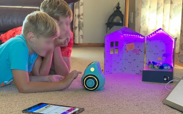 Two children watching a small robot beside its lit-up packaging
